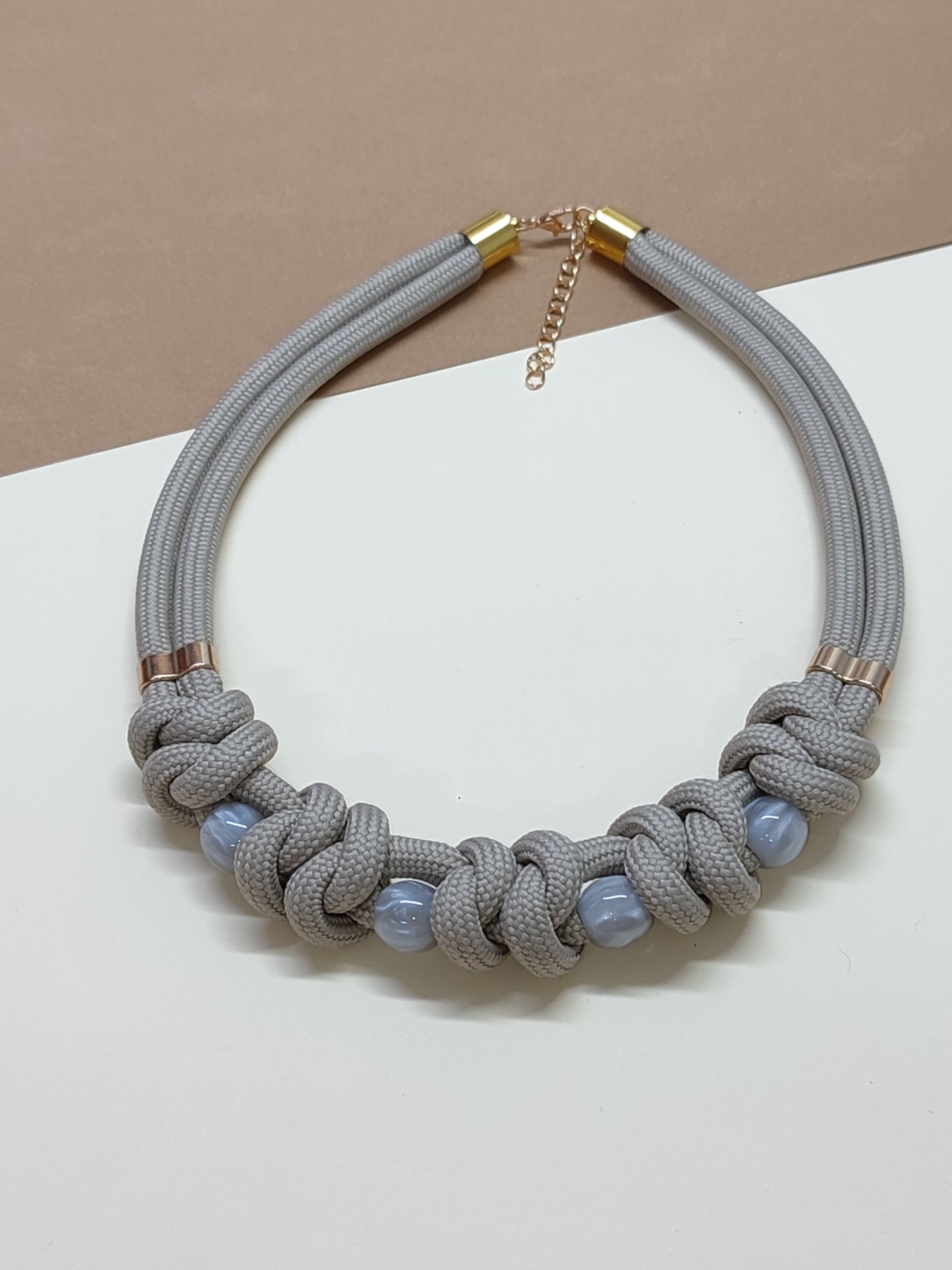 Colar estilo gargantilha modelo Malha com trançado plano horizontal de cordão cinza claro e contas esféricas intercaladas no padrão.