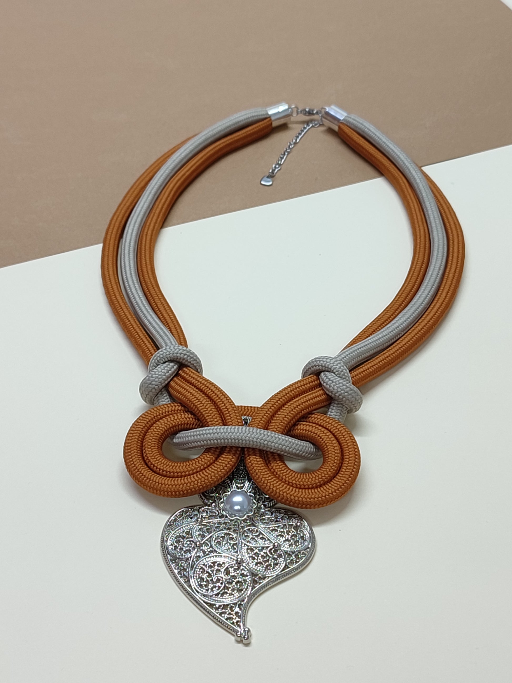 Colar de cordão artesanal modelo Laço com cordão em cores castanho e bege-prata e design simétrico de nós em espiral contínua com pendente ornamental de destaque na base