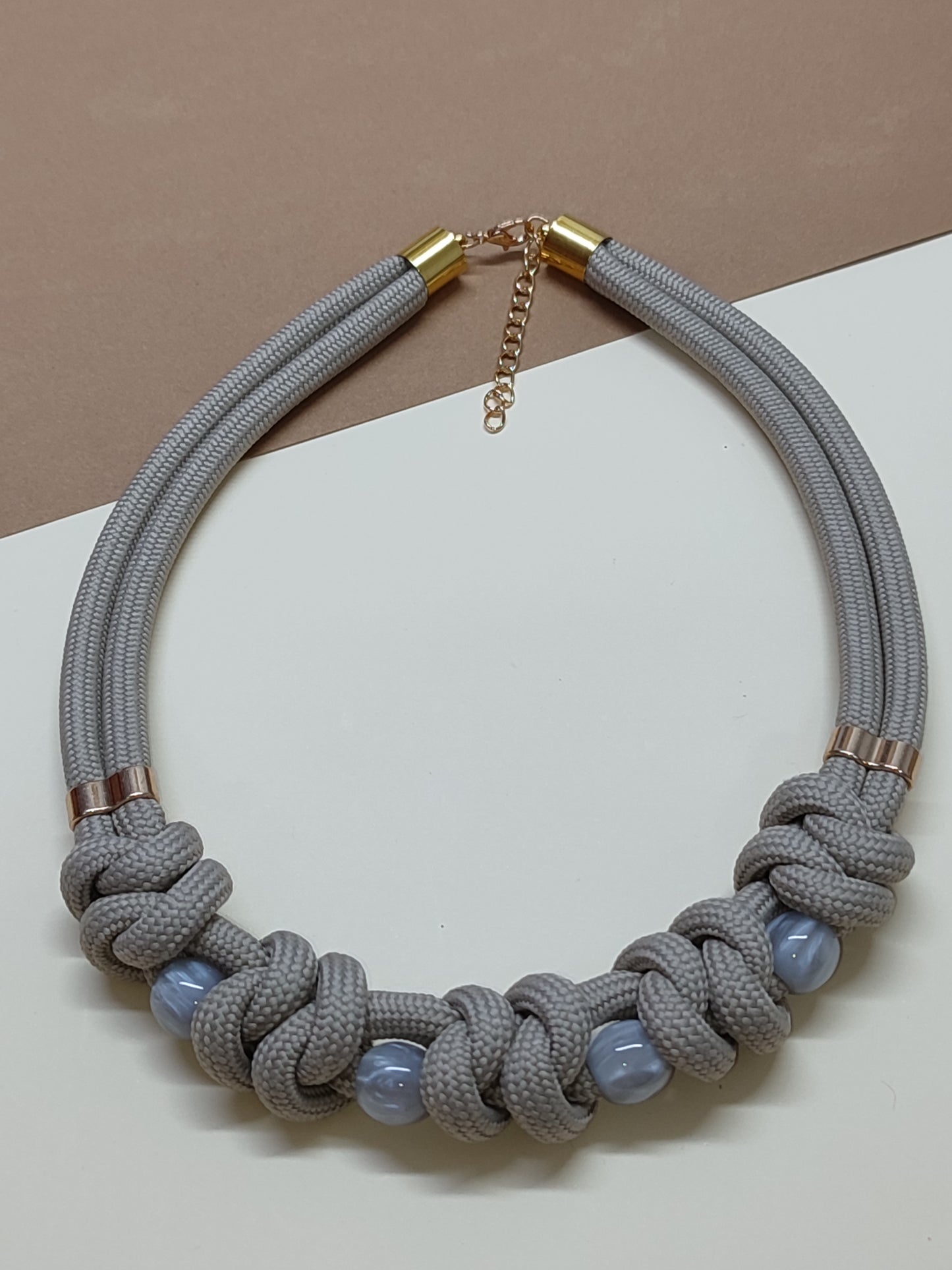 Colar estilo gargantilha modelo Malha com trançado plano horizontal de cordão cinza e contas esféricas intercaladas no padrão.