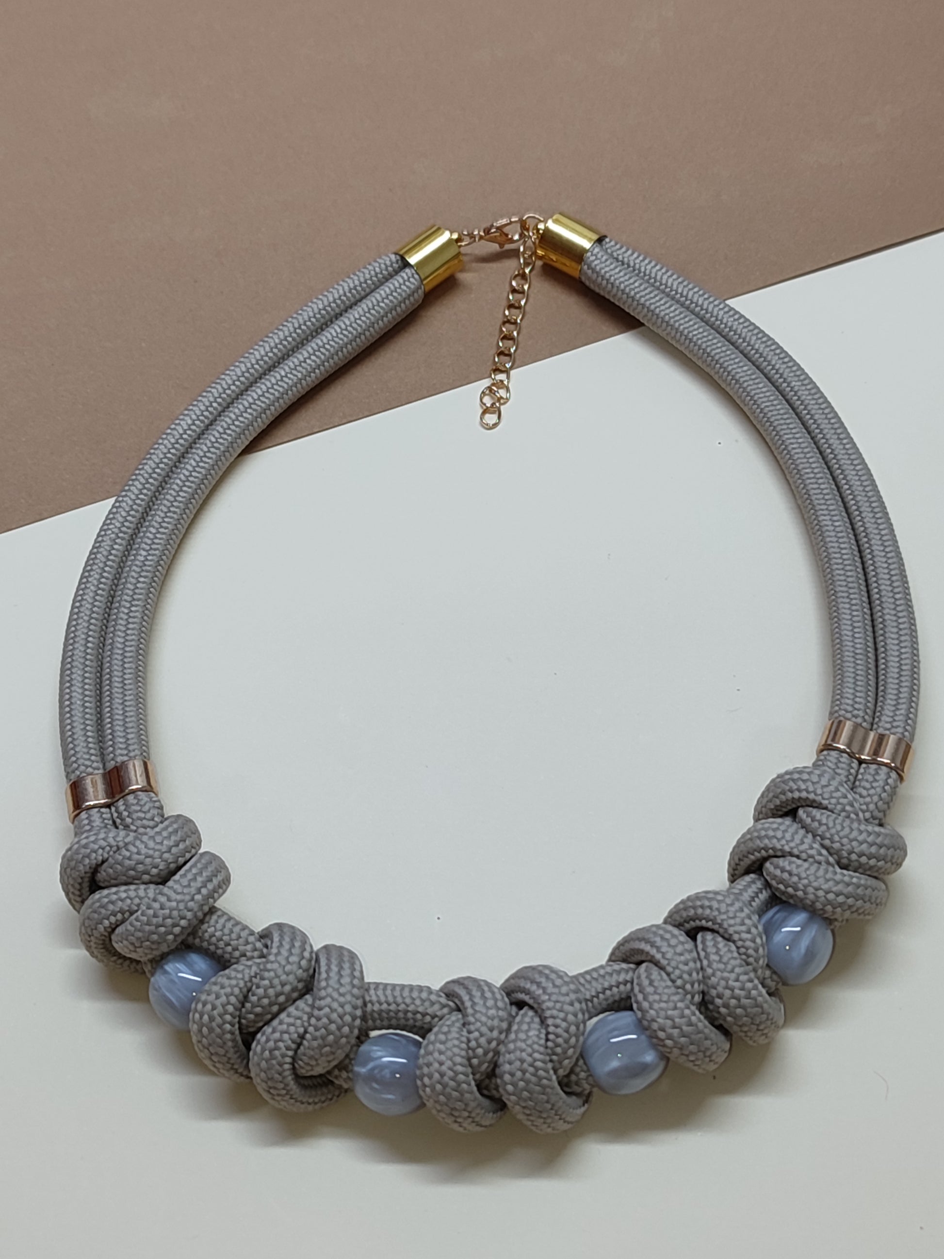 Colar estilo gargantilha modelo Malha com trançado plano horizontal de cordão cinza e contas esféricas intercaladas no padrão.