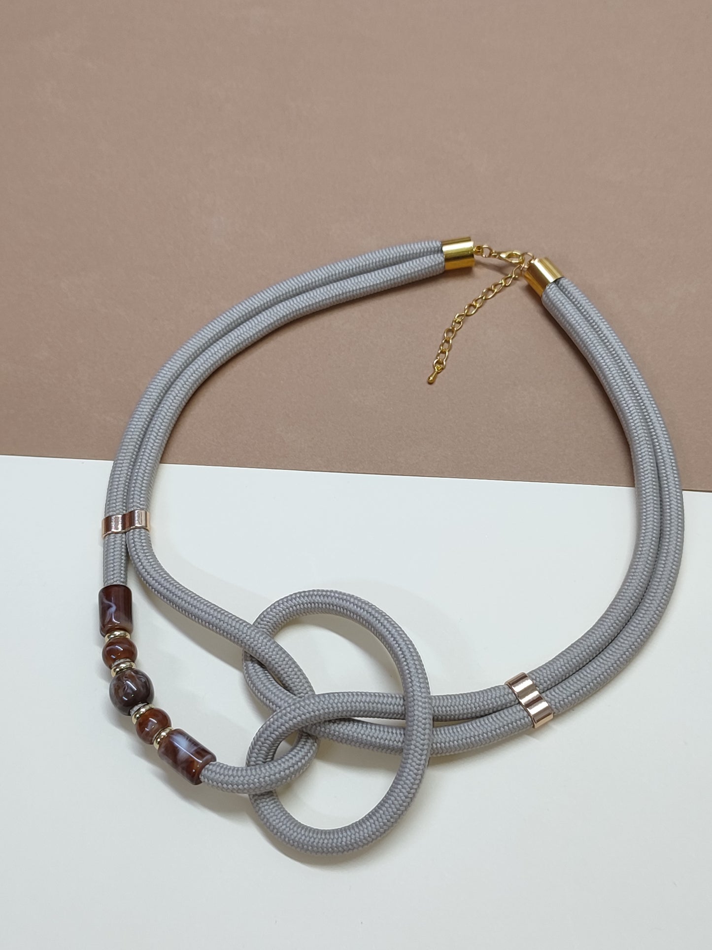 Colar de cordão grosso cinza-claro modelo Zira com nó artístico central e detalhe lateral de quatro contas ornamentais com efeito mármore castanho  dourado
