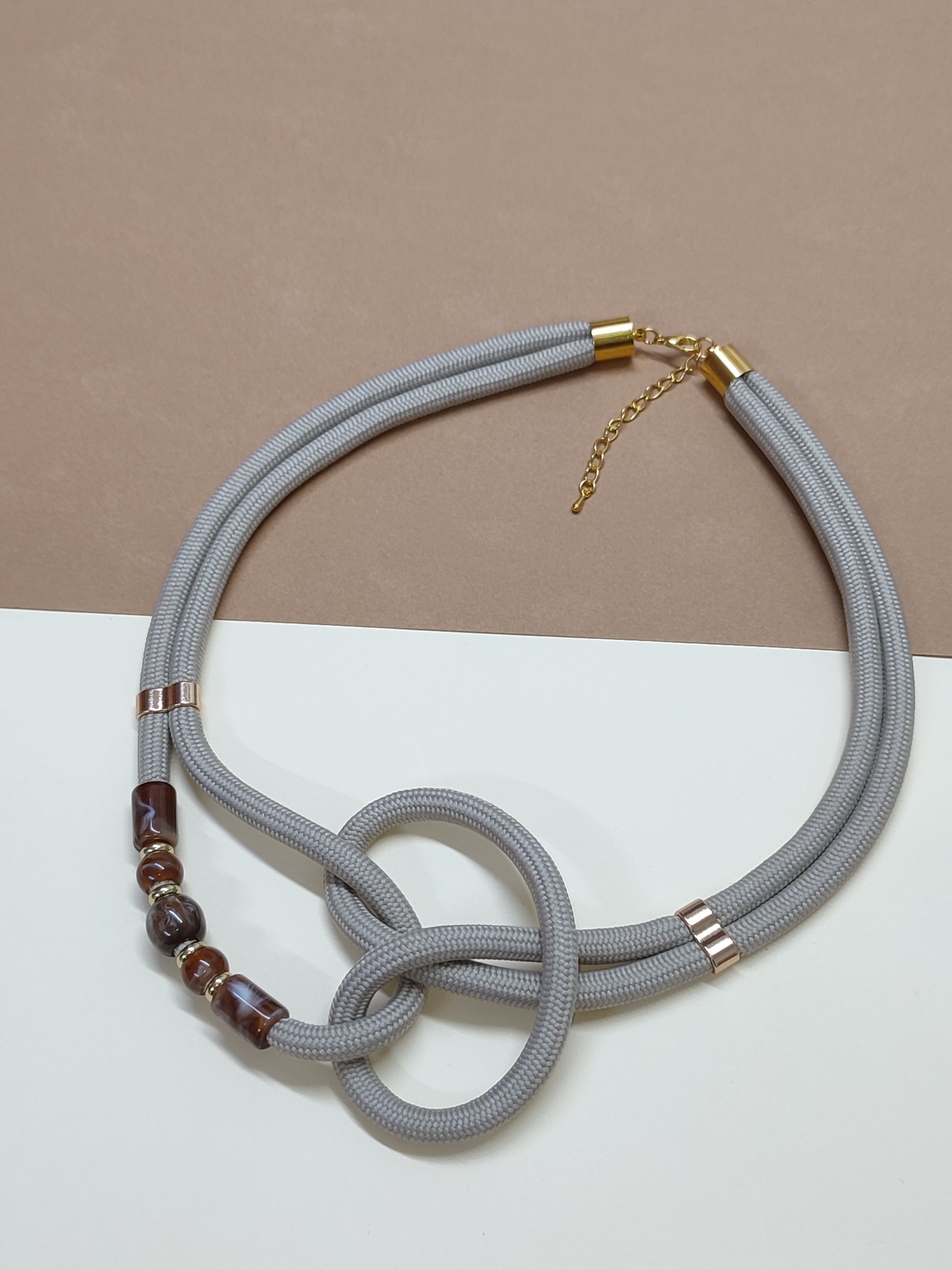 Colar de cordão grosso cinza-claro modelo Zira com nó artístico central e detalhe lateral de quatro contas ornamentais com efeito mármore castanho  dourado
